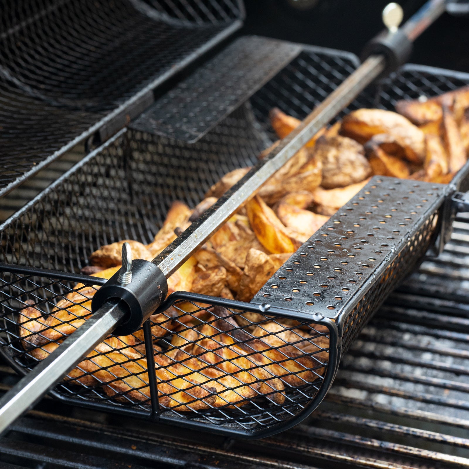 Grillkorb für Drehspieß gefüllt mit Kartoffel Wedges auf dem Grill