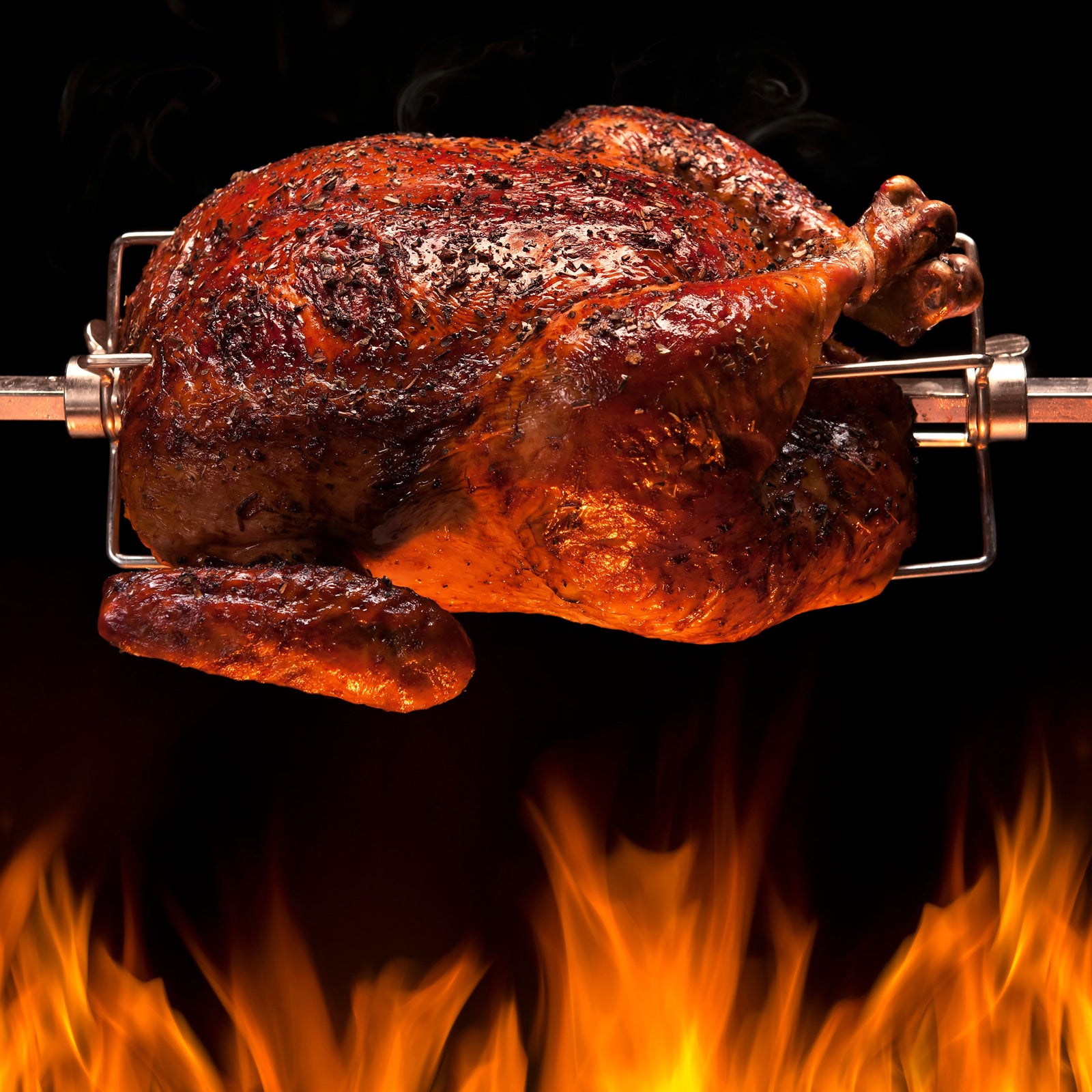 Ein knuspriges Grillhähnchen wird im Drehspieß über dem Feuer gegrillt