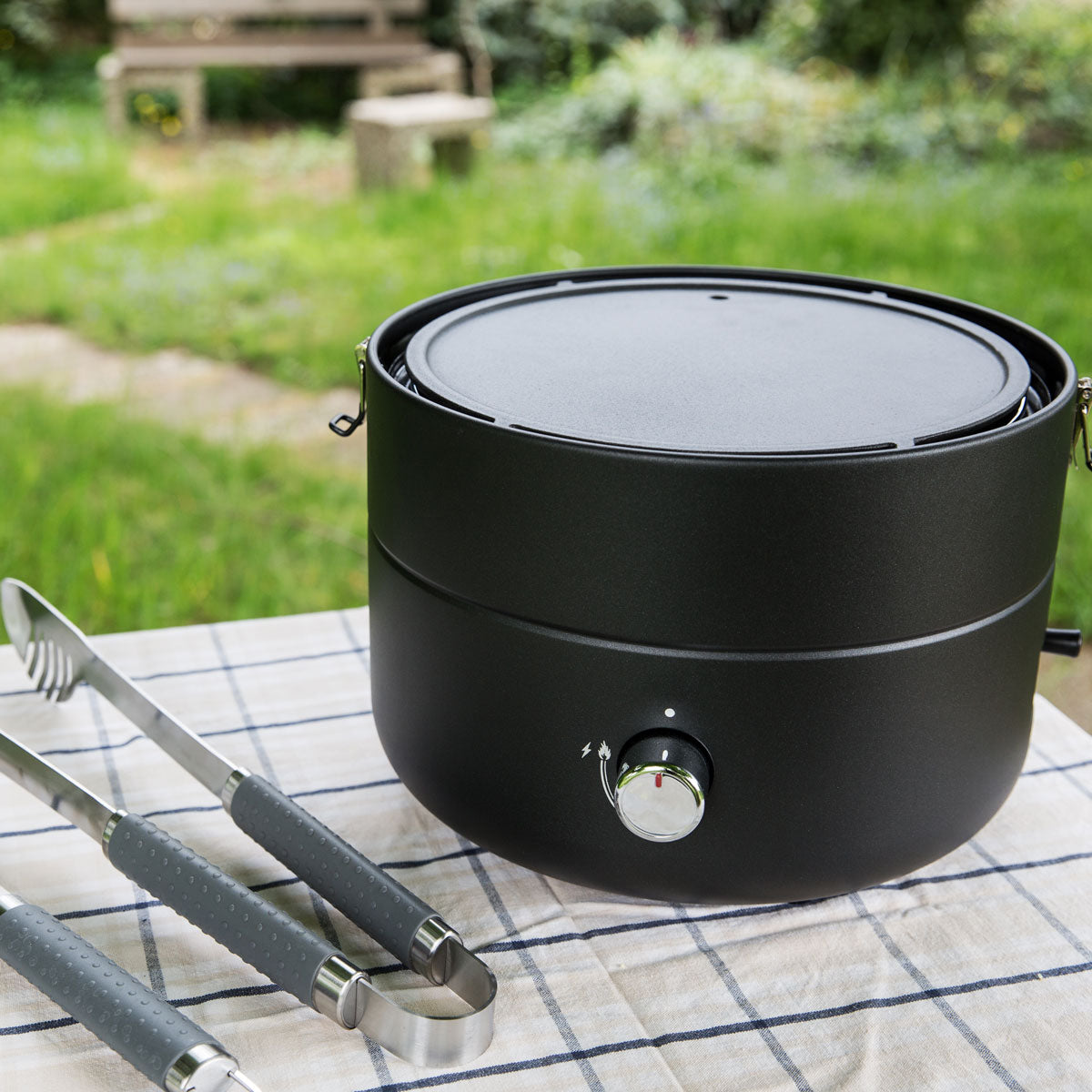 Der Grill-to-Go mit Gusseisen Grillplatte steht auf einem Tisch mit einer Grillzange daneben